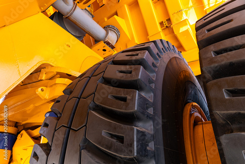 Tight detail view of large off-road tires mounted on a bright yellow industrial chassis. Visible tread pattern, wheel hub, suspension components and hydraulic