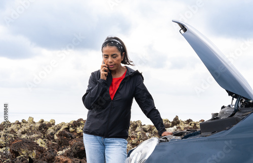 Foto Woman calling for help on a cell phone next to broken car with open hood, strand