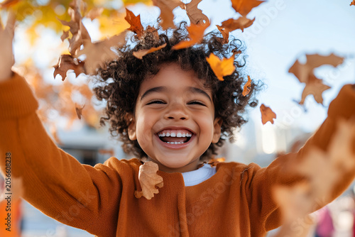 Joyful mixed ethnicity child playing with autumn leaves outdoors on a sunny day, throwing them into the air with a wide smile