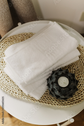 Minimalist still life of luxury spa essentials. White cotton towels with decorative candle on a table.