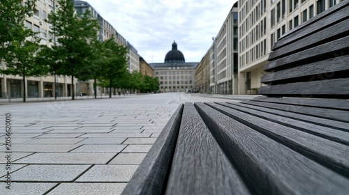 Low-angle view of a city plaza with a bench in the foreground, leading to a grand building