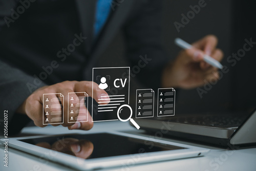A businessperson reviews digital resumes using a laptop and tablet, highlighting modern recruitment and job application processes.