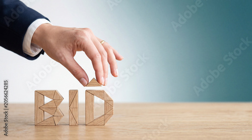 Business bidding and auction concept with wooden blocks spelling BID on a wooden table with ample copy space and a businessman hand