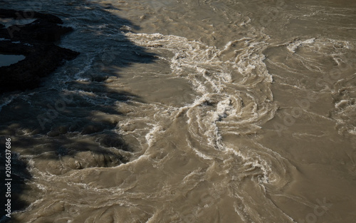 Aerial shot captures the texture of rushing, silt-heavy brown water with swirling eddy currents