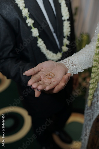 Traditional Indonesian wedding ceremony showing hands holding gold rings