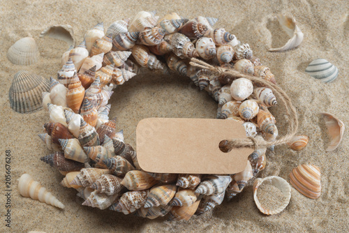 Arrangement of colorful seashells in the sand with a cardboard sign and space for text