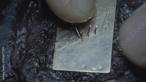 Hand engraving elegant cursive script letters into gold jewelry pendant closeup macro detail
