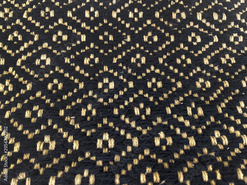 Close-up of a black and beige woven textile featuring a repeating geometric pattern. Detailed fabric texture with intricate craftsmanship, ideal as a background for design, decor, and textile themes.