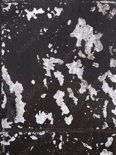 Abstract grunge metal texture with peeling white paint on a dark rusted surface. Weathered industrial background showing age, corrosion, decay, and distressed patterns for creative design use.