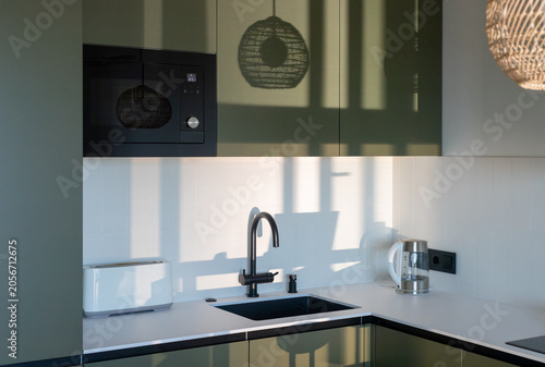 Tableau sur toile Modern kitchen interior with dark green glossy cabinets, built-in microwave, black sink and faucet, and white countertop