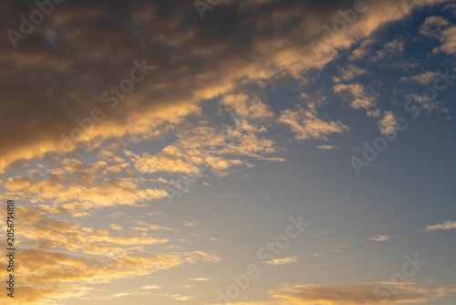 Sunset sky background with a band of golden orange altocumulus clouds across a blue sky. Warm dramatic cloudscape, nature background..