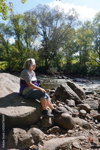 senior woman sitting on a rock by kabir kouba river