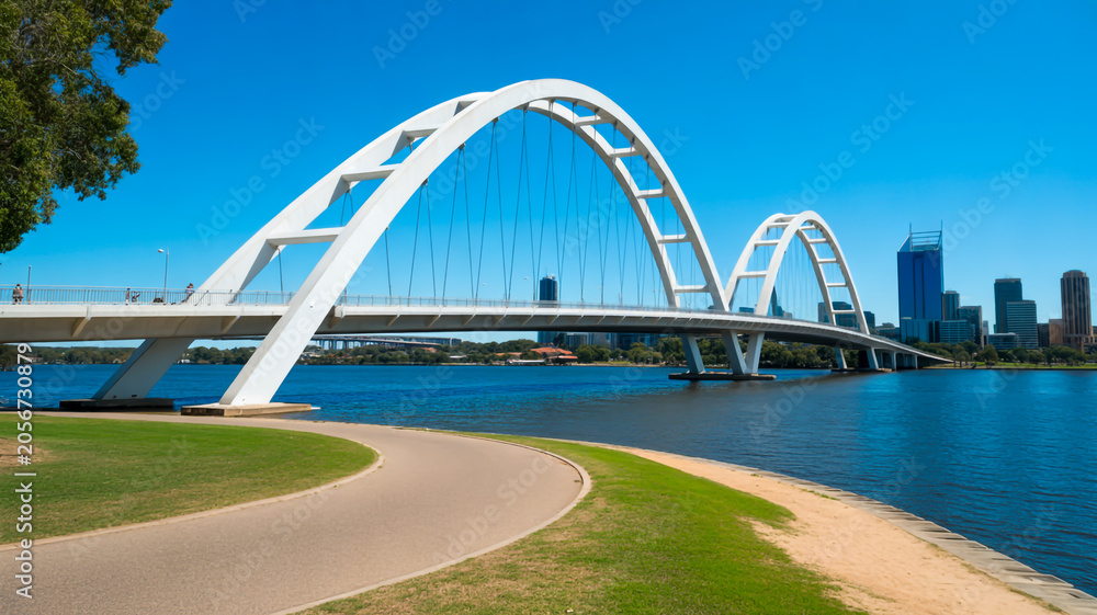 Fototapeta premium A scenic view of a bridge spanning a river with a cityscape in the background and a pathway leading to it.