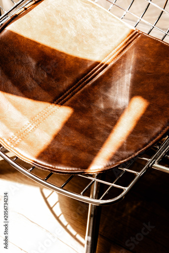 Brown leather chair with chrome wire frame, warm sunlight and glossy texture