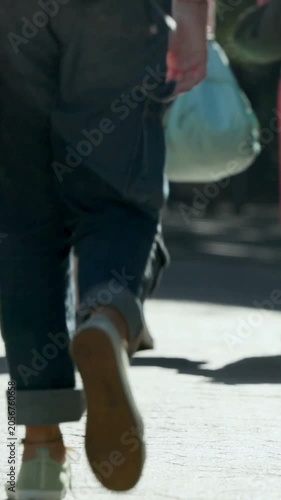 Vertical video: Walking woman going as camera starting low on sunlit path, mint tote and leggings