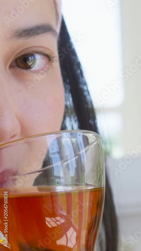 Vertical video: Lifting glass of tea, woman sipping at kitchen window, headband, plant, copy space