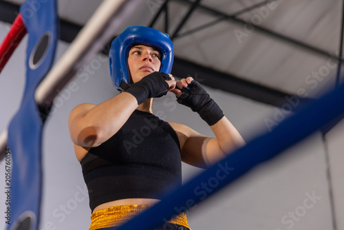Bild auf Leinwand Adult female boxer adjusting blue headguard securing wraps wearing crop top and
