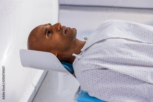 African American man lying supine on padded table in clinic gantry with headrest and hospital gown