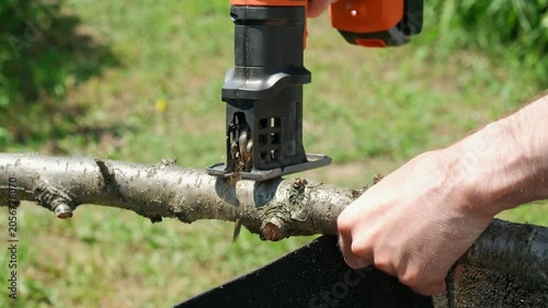 A close-up of a man cutting a branch with a jigsaw
