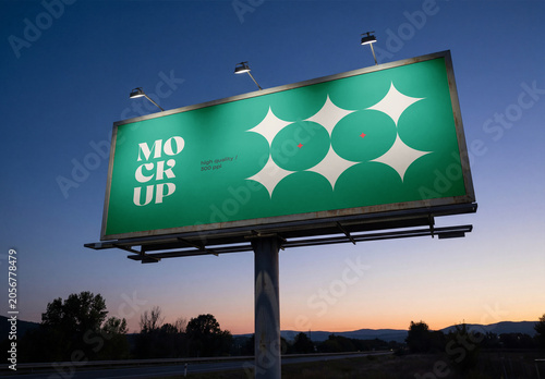 Low-angle perspective view of a massive outdoor billboard mockup with spotlights on a steel pillar structure next to a highway at sunset or twilight dawn