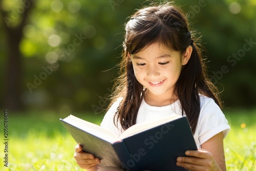 Child reading book on grass in outdoor park setting