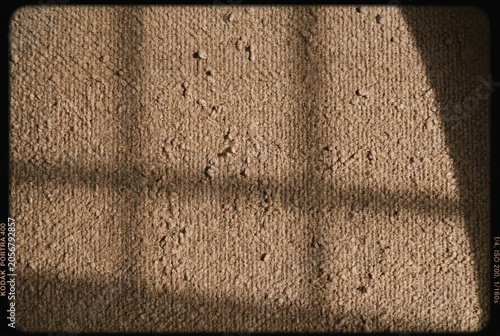 Textured light brown carpet with abstract shadow patterns, creating a tactile and warm background, showcasing natural textile fibers and a rough surface under sunlight