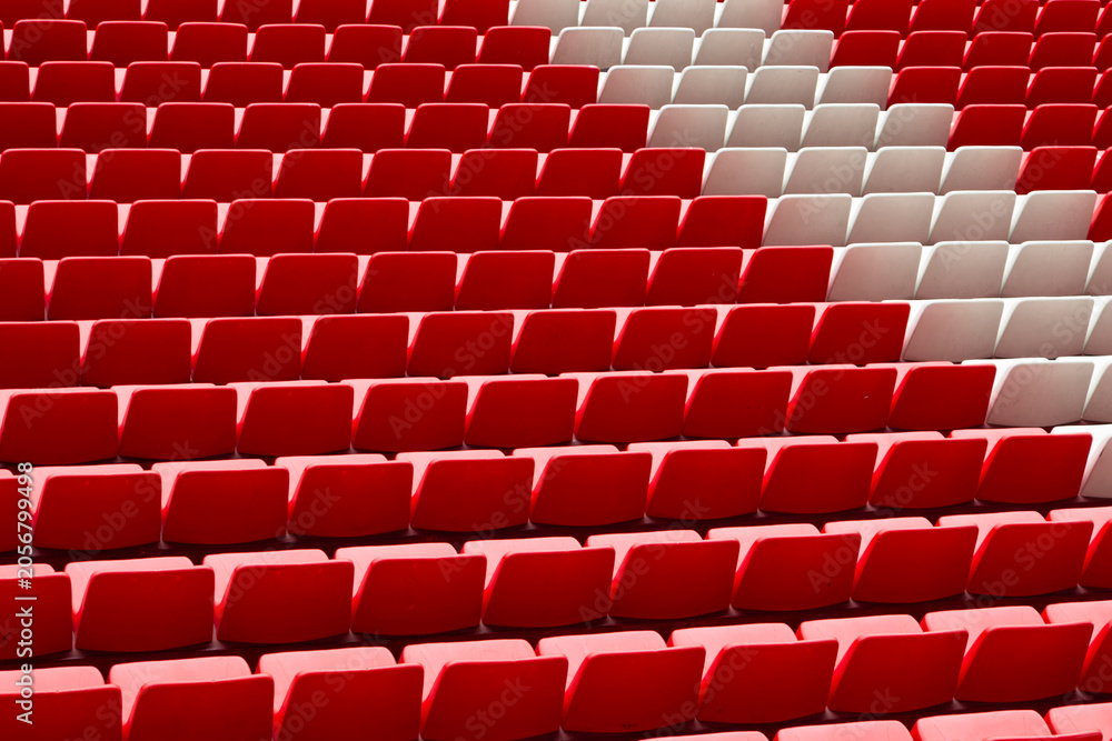 Fototapeta premium Empty red and white stadium seats in repeating rows create an abstract geometric pattern, evoking sports venues, empty grandstands, waiting spectators, and minimalist architecture