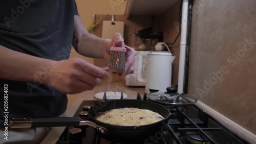 Cheese grater scene. Teen adds cheese to omelette. Morning kitchen moment with cheese being grated onto meal. Casual breakfast in small kitchen with hands grating cheddar onto freshly cooked dish