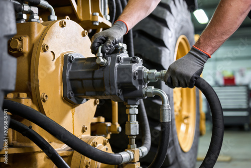Foto Mechanic wearing gloves connects hydraulic hose to heavy machinery pump