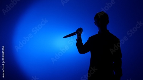 Cuadro en lienzo Silhouette of a man holding a sharp knife in dramatic blue backlight and spotlig