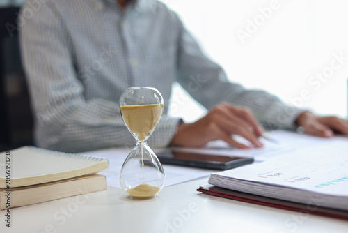 Obraz na płótnie Businessman at a desk with an hourglass in the foreground, representing a time management concept