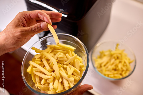 Hand placing fresh potato fries into a glass bowl near an air fryer
