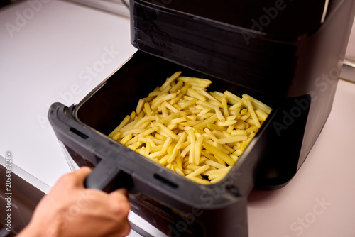 Hand placing fresh potato fries into a glass bowl near an air fryer
