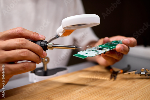 Man soldering electronic circuit on workbench under focused light