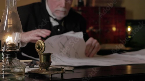 Focus on oil lamp of man sorting through large drawings