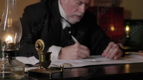 Focus on oil lamp of 19th century man writing with a dip pen