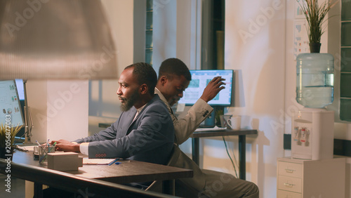 Photos Employee having fun at work during nightshift, bumping into coworker using desk chair, with friends racing eachother to avoid boredom during overnight stay in office