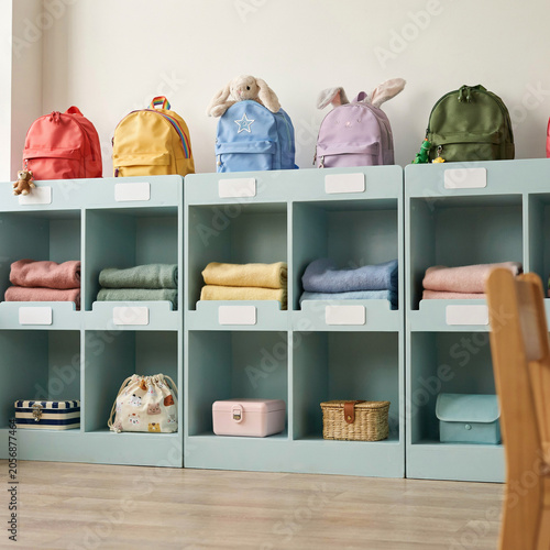 Backpacks and personal items occupy organized storage cubbies within a brightly lit elementary school classroom setting.