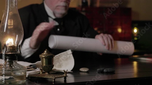 1800s man rolling up some large drawings focus on oil lamp