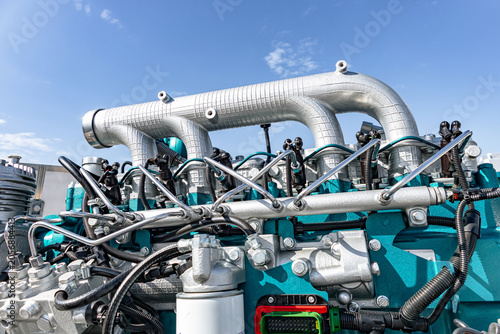 Close-up view of a large industrial diesel engine assembly showing metallic piping, turquoise-painted engine block, fuel lines, control valves and gauges