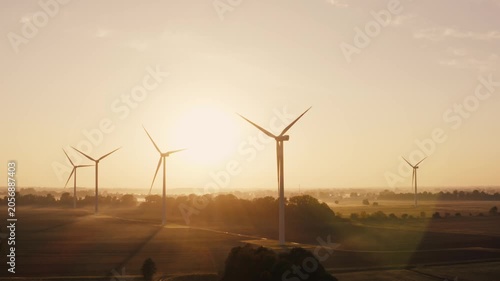 Golden rays illuminate a quiet field with wind turbines gently spinning. The tranquility of the early morning enhances the beauty of this serene landscape