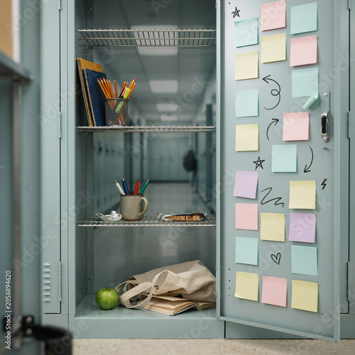 School locker stands open revealing a collection of academic supplies and colorful sticky notes attached to the door.