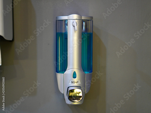 Cuadro en lienzo A wall-mounted silver and clear plastic liquid soap dispenser filled with blue g