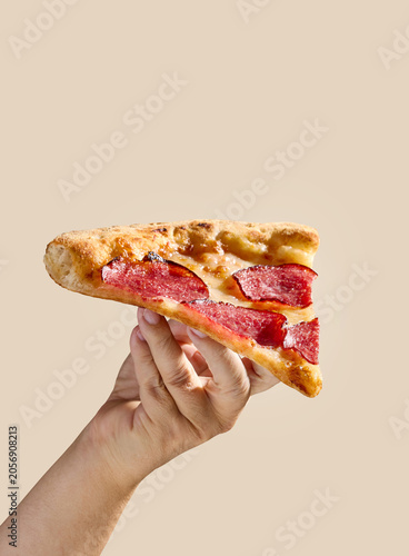 Hand Holding a Slice of Pepperoni Salami Pizza on Bright beige Background