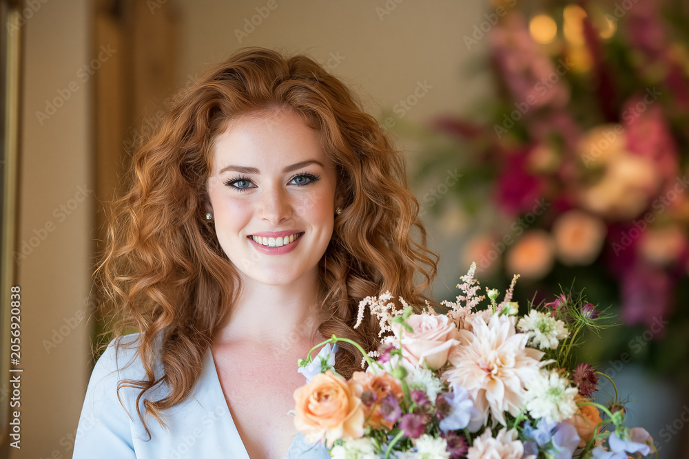 Fototapeta premium Smiling young woman with red curly hair holding a fresh pastel flower bouquet, celebrating beauty and joy
