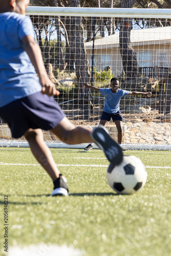 African American boys wearing light blue tees, navy shorts, kicking on turf toward goal with ball