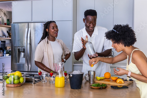 African American friends preparing cocktails at kitchen island, using clear bottle and metal shaker