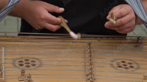 A street musician in a black T-shirt plays the ancient traditional national instrument, the dulcimer, with professional virtuosity and ease using wooden sticks