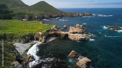 Aerial drone footage of the dramatic coastline at Point Lobos in Big Sur, California. The shot captures rugged cliffs, turquoise Pacific Ocean waves, rocky coves, and untouched natural landscapes.