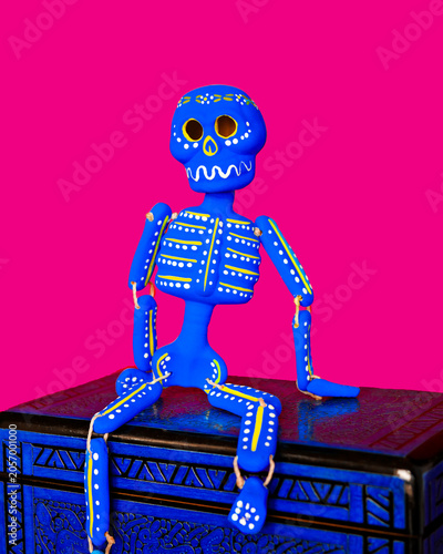 Colorful blue and yellow calaca sugar skull clay skeleton on a pink background